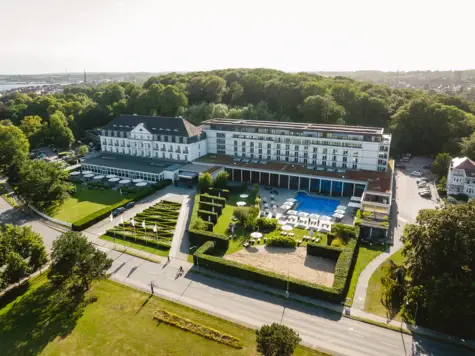 Großes weißes Gebäude mit Pool und Bäumen im Vordergrund.