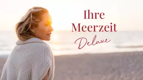 Eine Frau blickt entspannt über ihre Schulter, während sie an einem sonnigen Strand steht. Die goldene Stunde beleuchtet ihr Gesicht und ihren gestrickten Pullover. Der Text 'Ihre Meerzeit Deluxe' ist in Rot über dem Bild platziert.