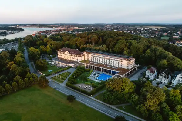 A-ROSA Travemünde Das A-ROSA Travemünde mit Pool, umgeben von Bäumen.