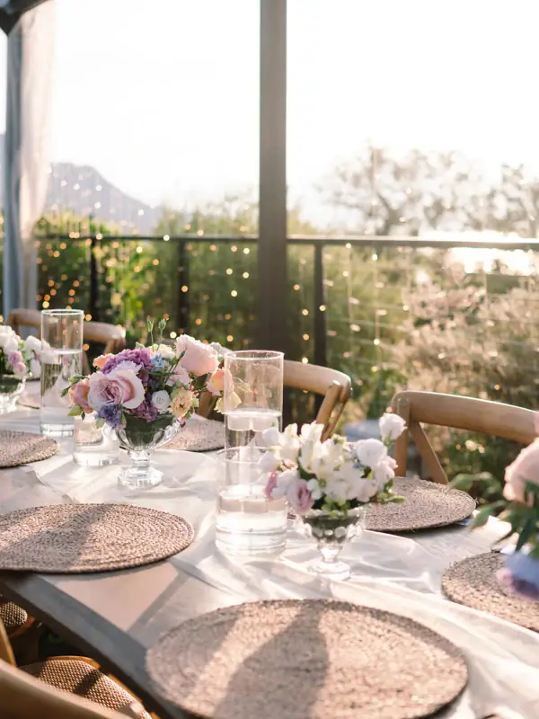 Festlich gedeckter Tisch im Freien mit weißen Tellern, geflochtenen Platzsets und zarten Blumenarrangements.