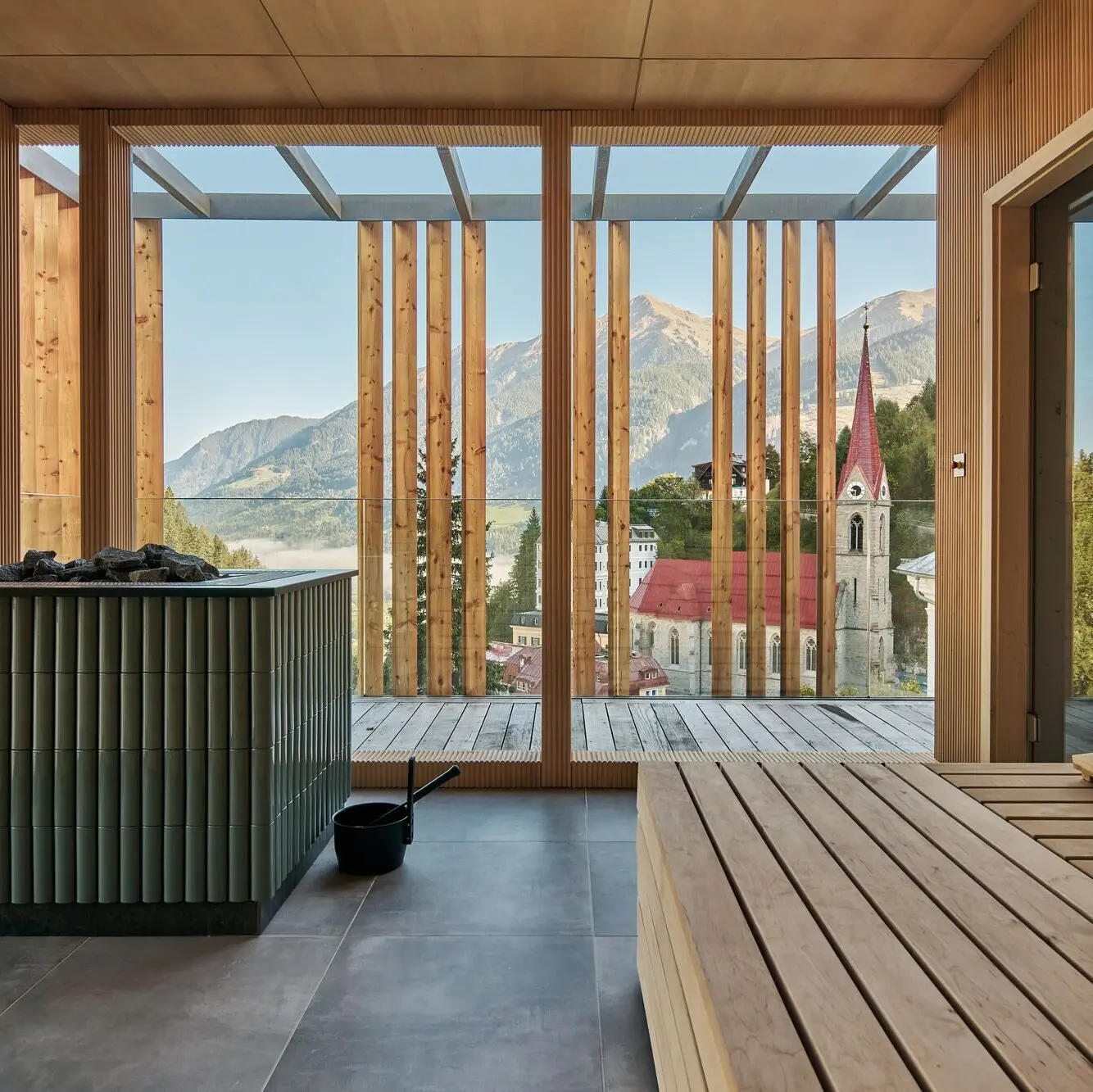Blick aus der Sauna auf das Tal. Im Vordergrund Sitzbänke, dann der Saunaofen und die holzverkleidete Fassade