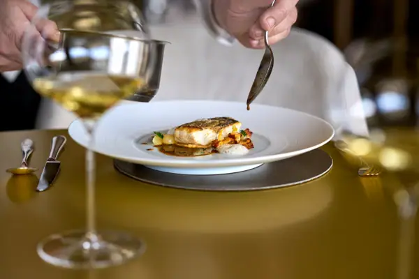 Eine Person hält einen Löffel über Essen auf einem Teller.