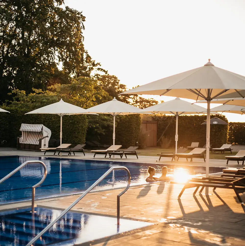 Eine Person im Pool mit Sonnenschirmen und Liegestühlen.