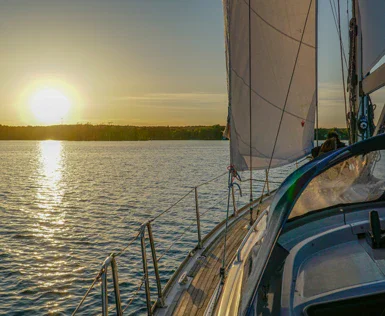 Ein Segelboot segelt in Richtung Sonnenuntergang. Das Meer ist ruhig und spiegelt die goldene Sonne. 