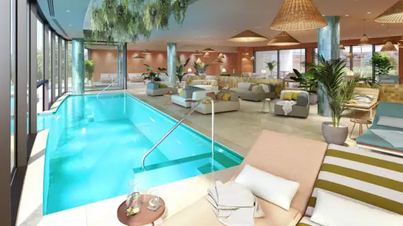 Photorealistic representation of an indoor swimming pool in a spa facility. The indoor pool is filled with clear, turquoise blue water and a large glass front provides plenty of natural light. Hanging gardens above the pool create a green oasis. The lounge area is furnished with modern sofas and armchairs, above which large, woven hanging lamps hover. The design is a harmonious blend of natural tones and textiles that create a relaxing atmosphere.