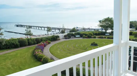 Blick von einem Balkon auf einen Garten und eine Seebrücke, die in die Ostsee ragt..