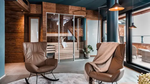 Two brown leather armchairs stand on a gray carpet and a sauna and access to a terrace can be seen in the background. 