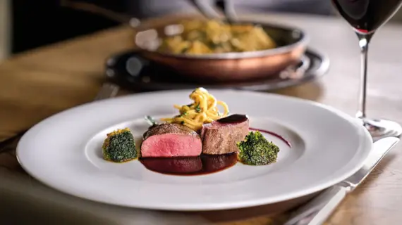 A plate of food on a table, accompanied by a wine glass filled with red wine.