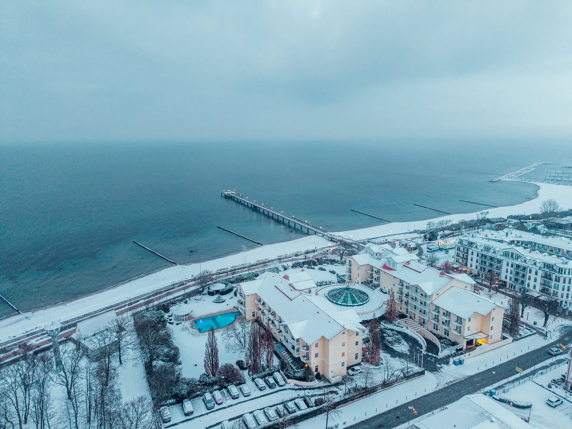 Schneebedeckter Strand mit Gebäuden und einem Pier im Winter.