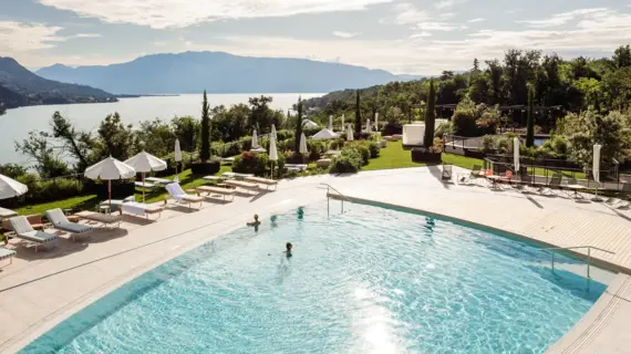 Ein Swimmingpool umgeben von Bäumen unter einem teilweise bewölkten Himmel, in dem zwei Personen schwimmen.