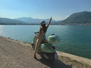 Frau auf einem Roller am Ufer des Gardasees.