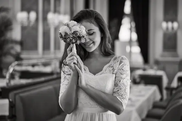 Frau in einem Hochzeitskleid hält Blumen vor ihrem Gesicht.