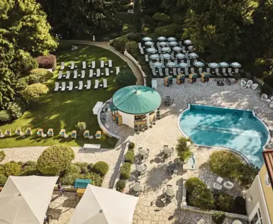 Idyllischer Wellnessbereich mit gepflegtem Garten, Liegestühlen, Sonnenschirmen und einem Außenpool. Ein Pavillon mit grünem Dach und Sitzgelegenheiten lädt zum Verweilen ein, umgeben von üppiger Vegetation.