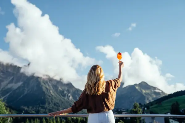 Eine Frau hält einen Drink in die Luft und schaut auf die Berge.