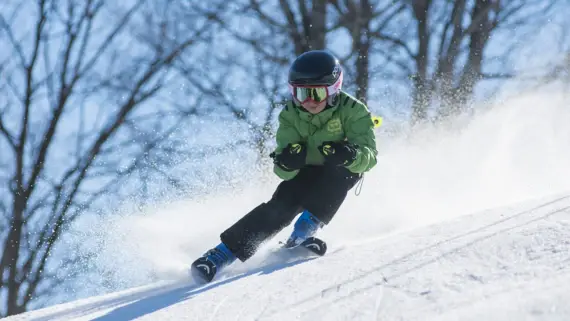 A little boy in a green jacket skis towards the camera.