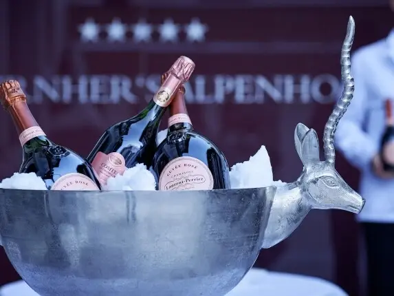 A large metal bowl is filled with ice and 3 champagne bottles.