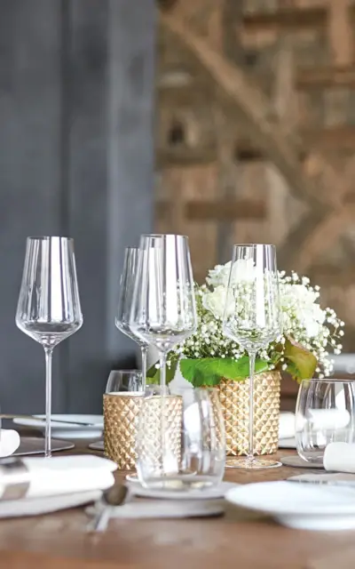 Elegant gedeckter Tisch mit Weingläsern und Blumenvase als Mittelstück.