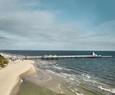 Long pier extending into the ocean with cloudy skies above.