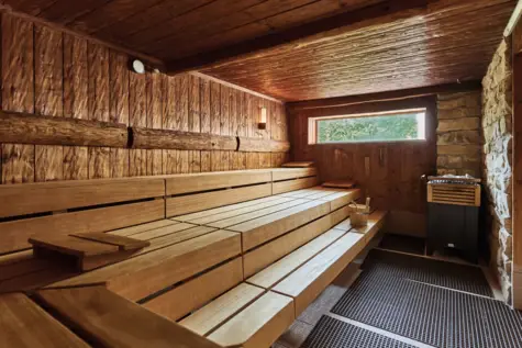 Eine Holzsauna mit unterschiedlichen Holzelementen und einem kleinen, länglichen Fenster mit Blick ins Grüne. 