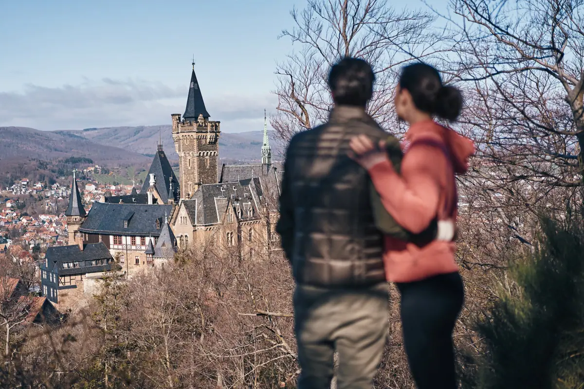 Ein Mann und eine Frau stehen auf einem Hügel und blicken auf das Wernigerode Schloss.