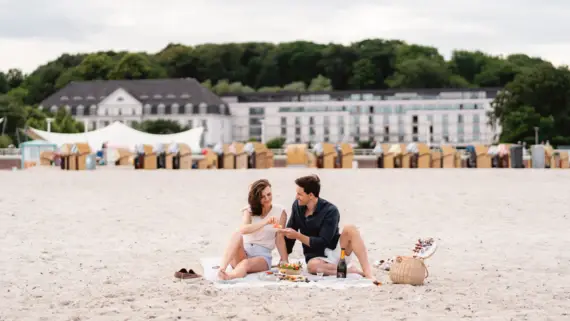 Ein Mann und eine Frau sitzen auf einer Decke am Strand und Picknicken.