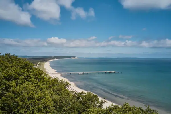 Strand mit einem Pier und Bäumen im Vordergrund.