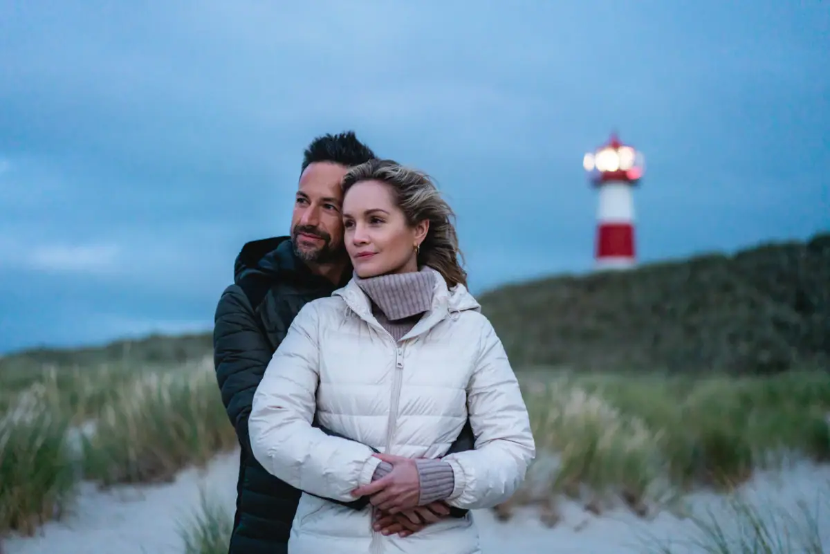 Ein Mann und eine Frau stehen am Strand mit einem Leuchtturm im Hintergrund.