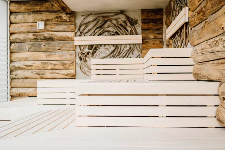  Das Innere einer Sauna, geprägt von einem interessanten Kontrast zwischen rauen, natürlichen Treibholzwänden und den glatten, hellen Holzbänken, die zum Entspannen einladen. Die Wände und die Decke zeigen ein kunstvolles Arrangement von Treibholzstücken, die eine rustikale und entspannende Atmosphäre schaffen.