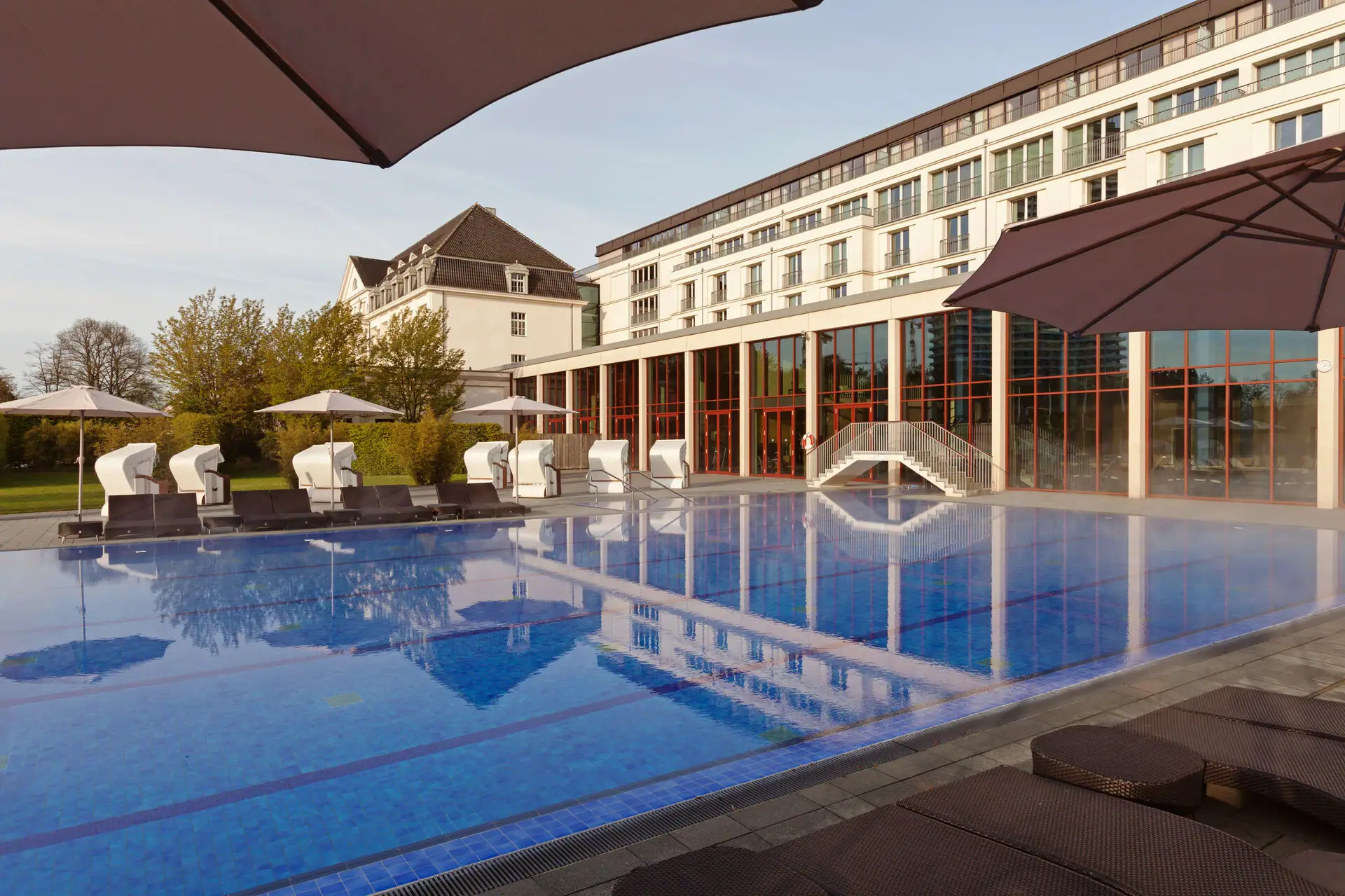 Ein Außenpool mit Sonnenschirmen und Liegestühlen vor dem A-ROSA Hotel in Travemünde.