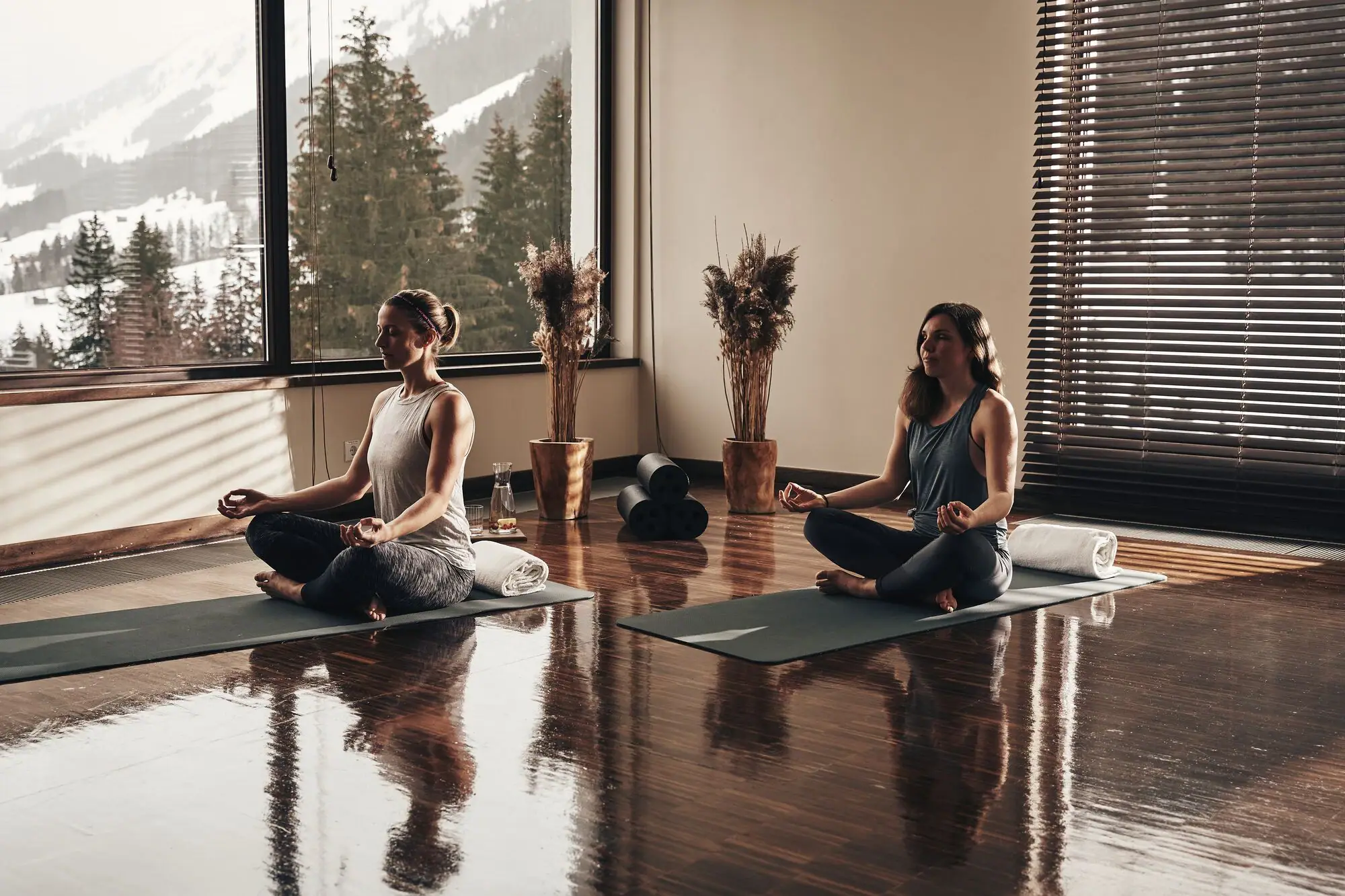 Eine Gruppe von Frauen sitzt auf Matten in einem Raum mit Fenstern und Blick auf die Berge.