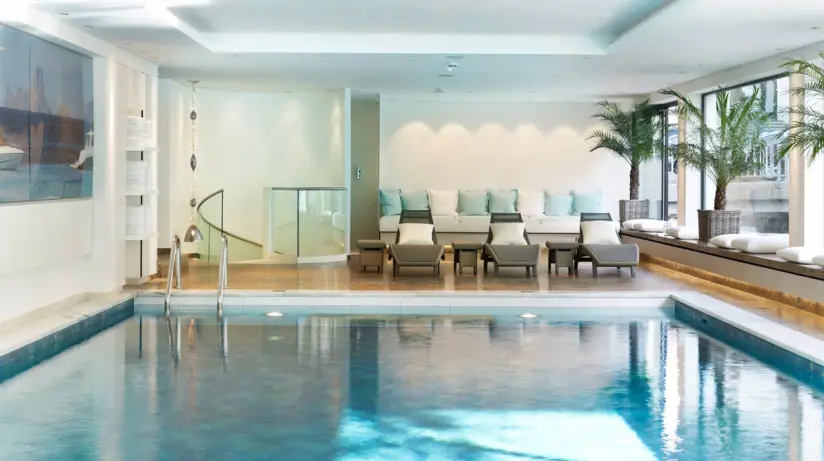 Indoor swimming pool with clear water, surrounded by chairs and elegant interior design.