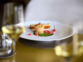 Elegant angerichtet steht ein Teller mit grüner Soße und einem kleinen Häppchen zusammen mit Weißweingläsern auf einem Tisch. 