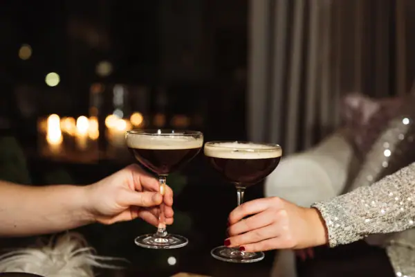 Hände halten Cocktailsgläse mit brauner Flüssigkeit