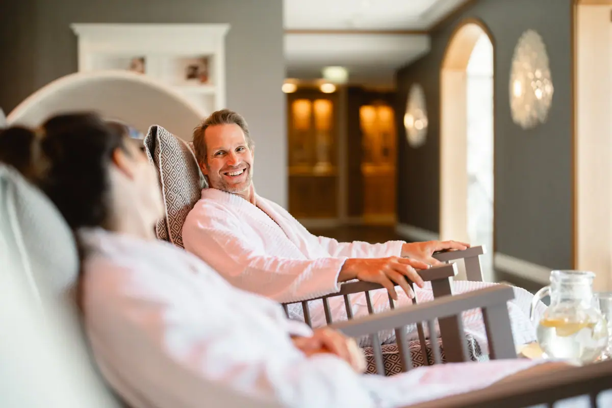 Ein Mann und eine Frau im Bademantel sitzen auf im Wellnessbereich in Relax-Sesseln.