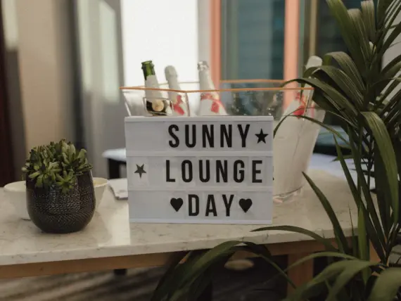 Ein Schild mit der Aufschrift "Sunny Lounge Day", dekoriert mit Pflanzen und Veuve Clicquot Luftballons.