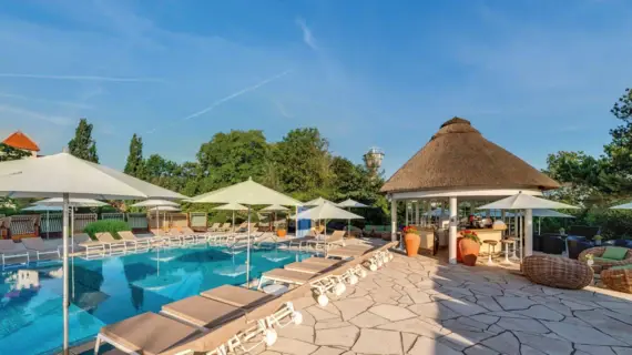 Außenbereich des SPA-ROSA Kühlungsborn mit Pool, Liegen und einer Poolbar in der Morgensonne. 