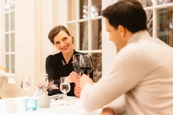 Ein Mann und eine Frau sitzen an einem Tisch mit Weingläsern und stoßen an.