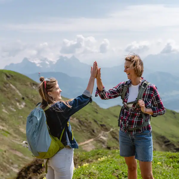 Zwei Frauen geben sich im Freien ein High Five und Berge sind im Hintergrund zu sehen..