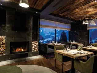 Ein gemütlicher und eleganter Restaurantbereich mit einem brennenden Kamin und Ausblick auf schneebedeckte Berge.