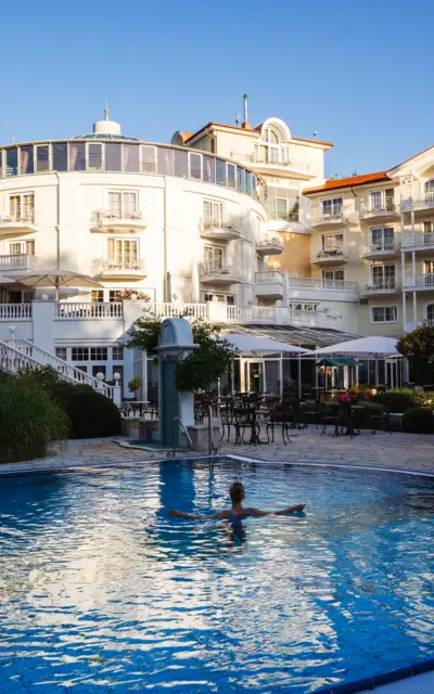 Eine Frau im Pool mit einem großen Hotel im Hintergrund.