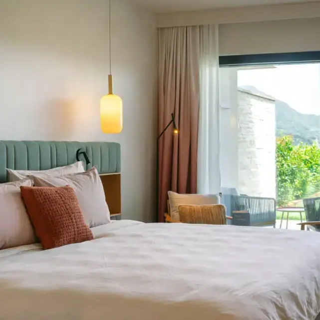 Hotelzimmer mit Bett, Stühlen und großer Schiebetür zum Garten.