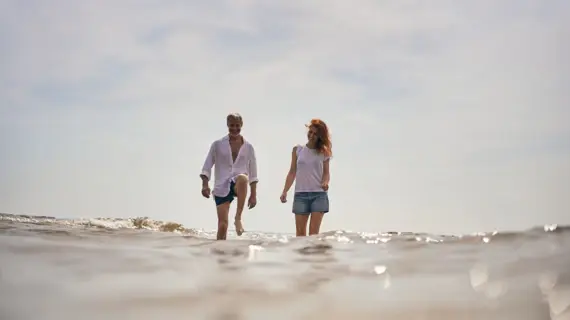 Ein Mann und eine Frau spazieren fröhlich durch das glitzernde flache Wasser der Ostsee.
