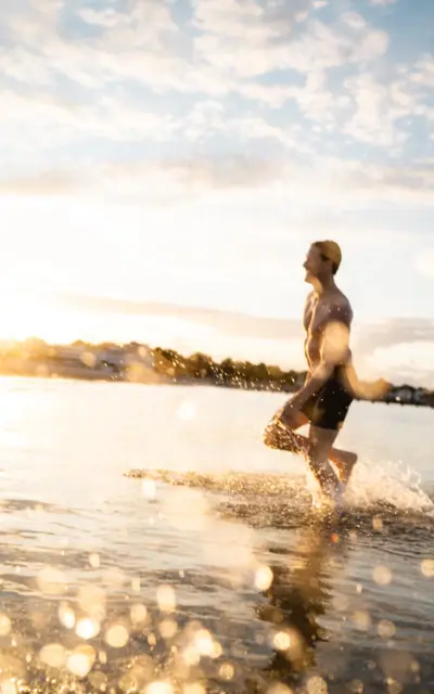 Mann läuft im Wasser an einem sonnigen Strand.