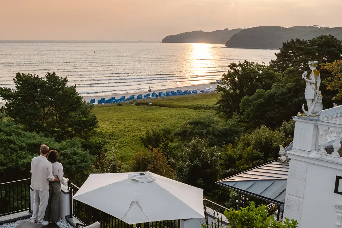 Frau steht auf einem Balkon mit Blick auf einen Strand.
