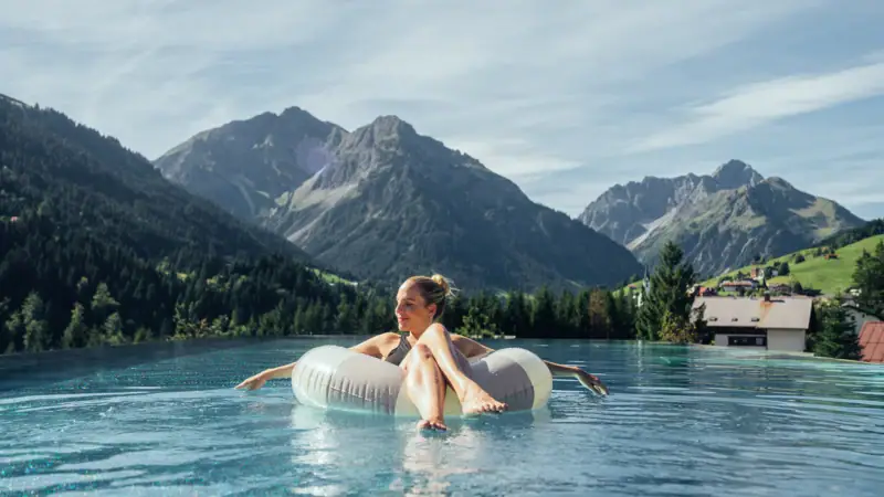 Eine Frau treibt auf einem Schwimmreifen in einem Pool mit Bergen im Hintergrund.