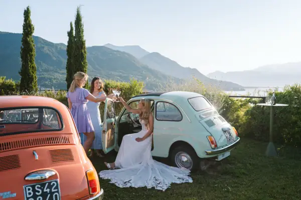 Hochzeitsgäste und Brautpaar feiern auf der Terrazzo 500 mit Fiat 500 und Blick über den Gardasee.