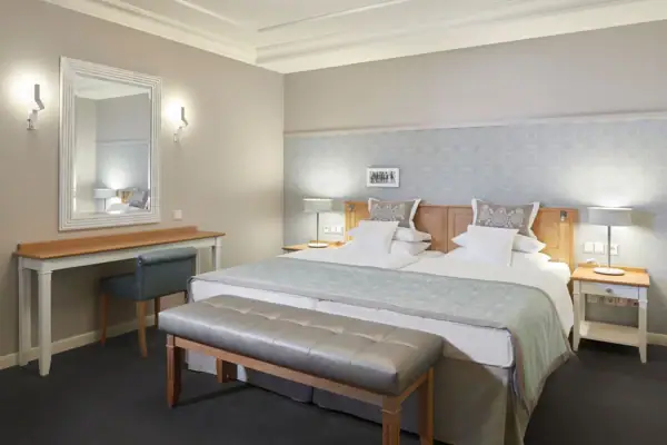 Hotelzimmer mit einem großen gemütlichen Bett und einem Spiegel an der Wand daneben.