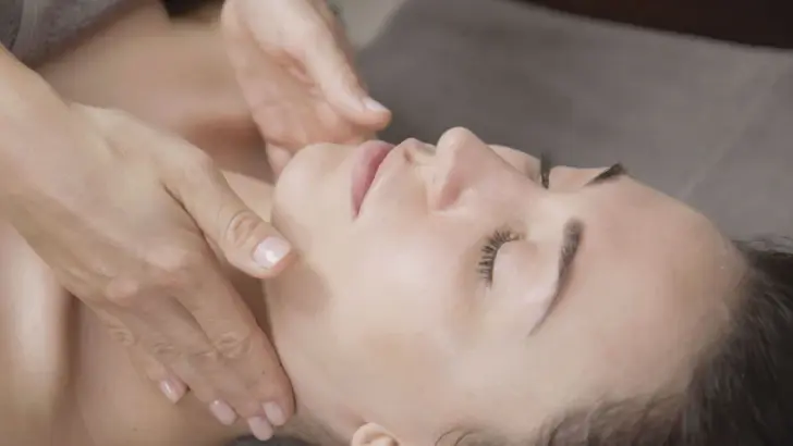 A facial massage during a wellness treatment, with gentle finger movements massaging the forehead of a relaxed woman with her eyes closed. The close-up focuses on the professional strokes of the masseuse, who gently touches the woman's face and creates a calming atmosphere.