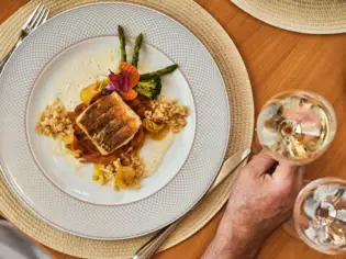 Ein Teller mit Essen und eine Hand, die ein Glas Wein hält.