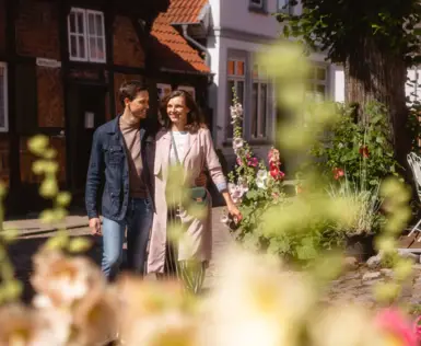 Eine Frau und ein Mann gehen zusammen durch die Altstadt von Travemünde. Im Hintergrund sind alte Fachwerk-Häuser zu erkennen.
